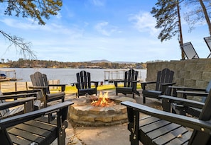 A lakeside seating area with Adirondack chairs and a stone fire pit.