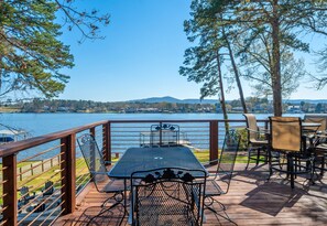 A deck with a table and chairs overlooking a lake, surrounded by trees and a distant mountain. - Modern Lakefront Escape | Private Dock | Hot Tub (Hot Springs)