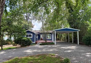 A house with a covered porch, surrounded by trees and a gravel driveway. - Modern Lakefront Escape | Private Dock | Hot Tub (Hot Springs)