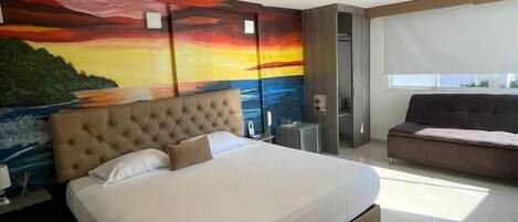 A modern bedroom with a large bed, a mural on the wall, a sofa, and a window.