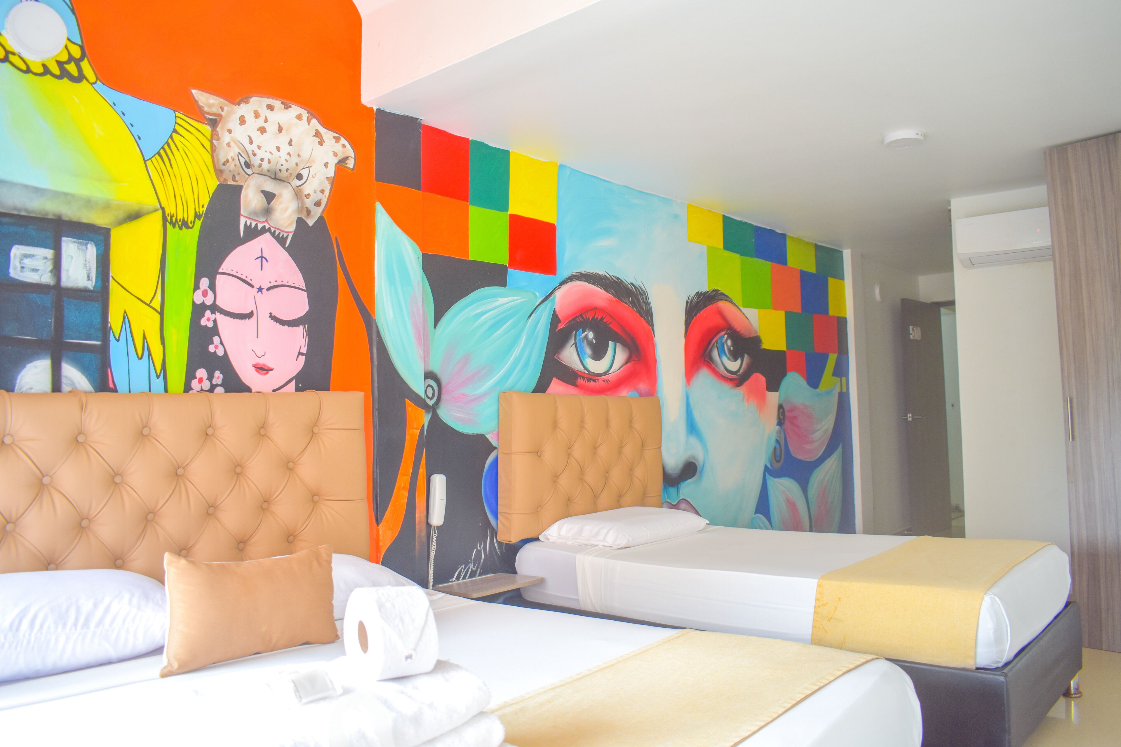 Una habitación de hotel con dos camas, un mural grande y colorido en la pared y un diseño moderno.