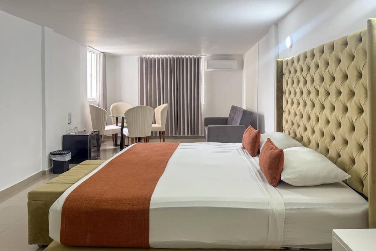 Habitación de hotel con una cama grande, una mesita de noche, una silla, un escritorio y una ventana con cortinas.