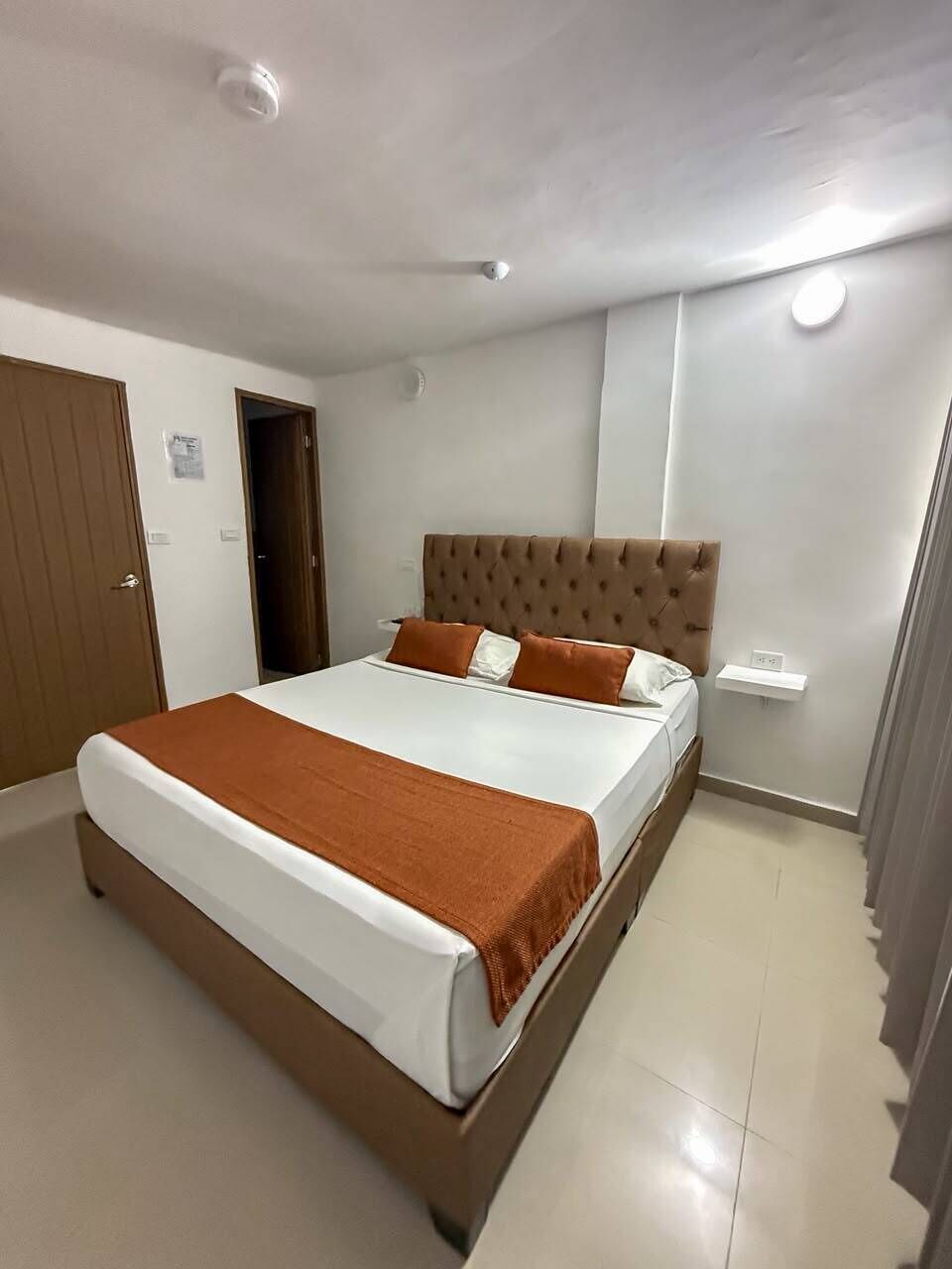 A bedroom with a bed, a door, a light switch, and a wall socket.