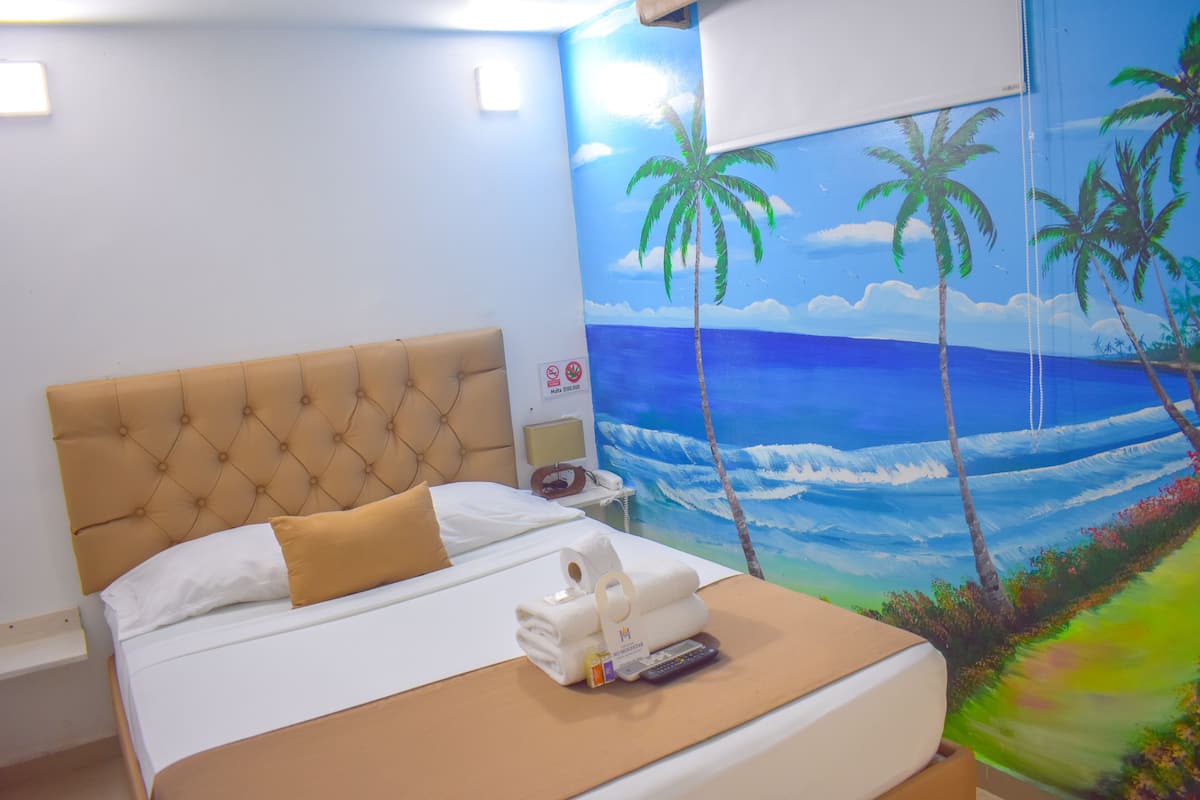 Habitación de hotel con cama, mesita de noche, un cuadro de una playa y un letrero que indica prohibido fumar.