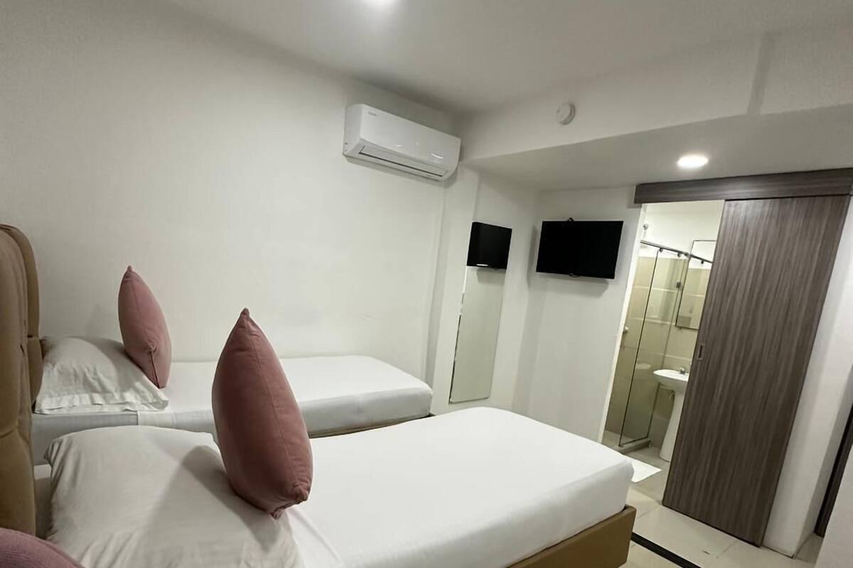 Una habitación de hotel con dos camas, aire acondicionado, televisor y baño con ducha y lavamanos.