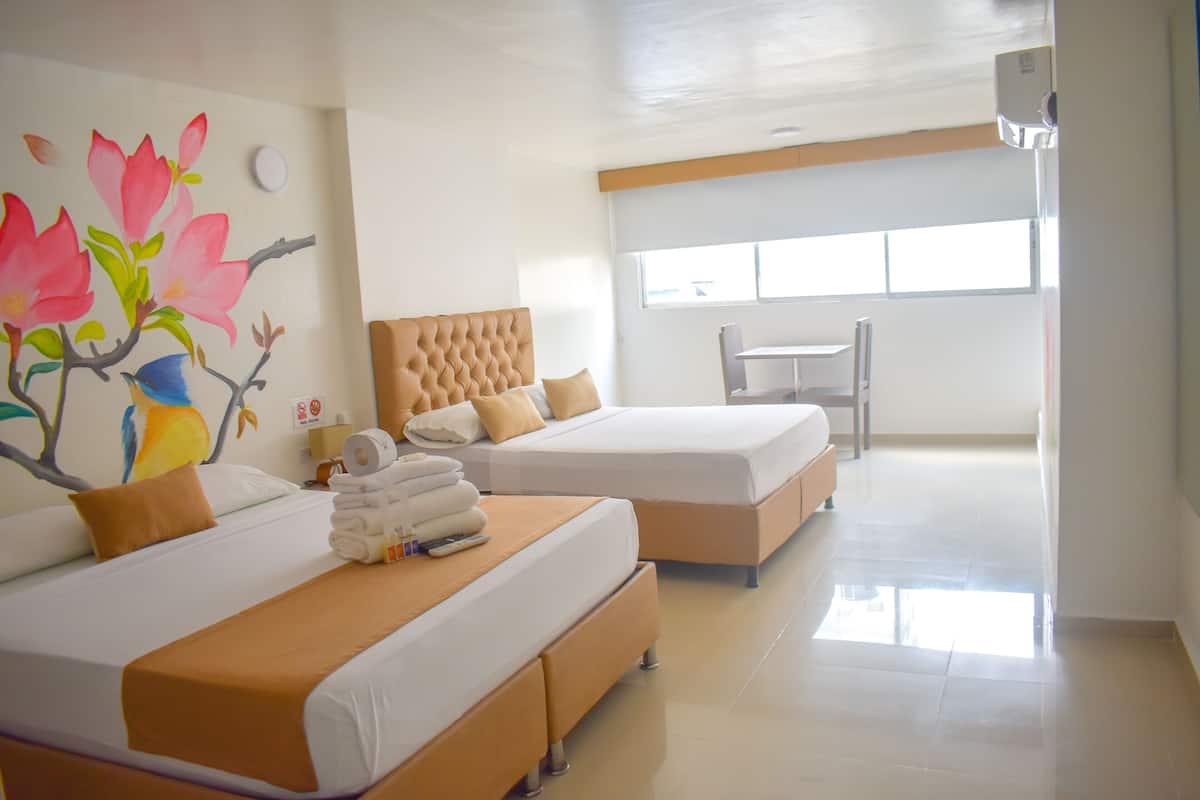 Habitación de hotel con dos camas, un cuadro de pájaros y flores en la pared, una ventana y una mesa.