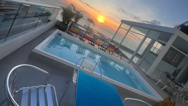 A rooftop pool with glass railings, a view of the sunset, and outdoor seating. - Hotel Hernandez CTG (Cartagena)