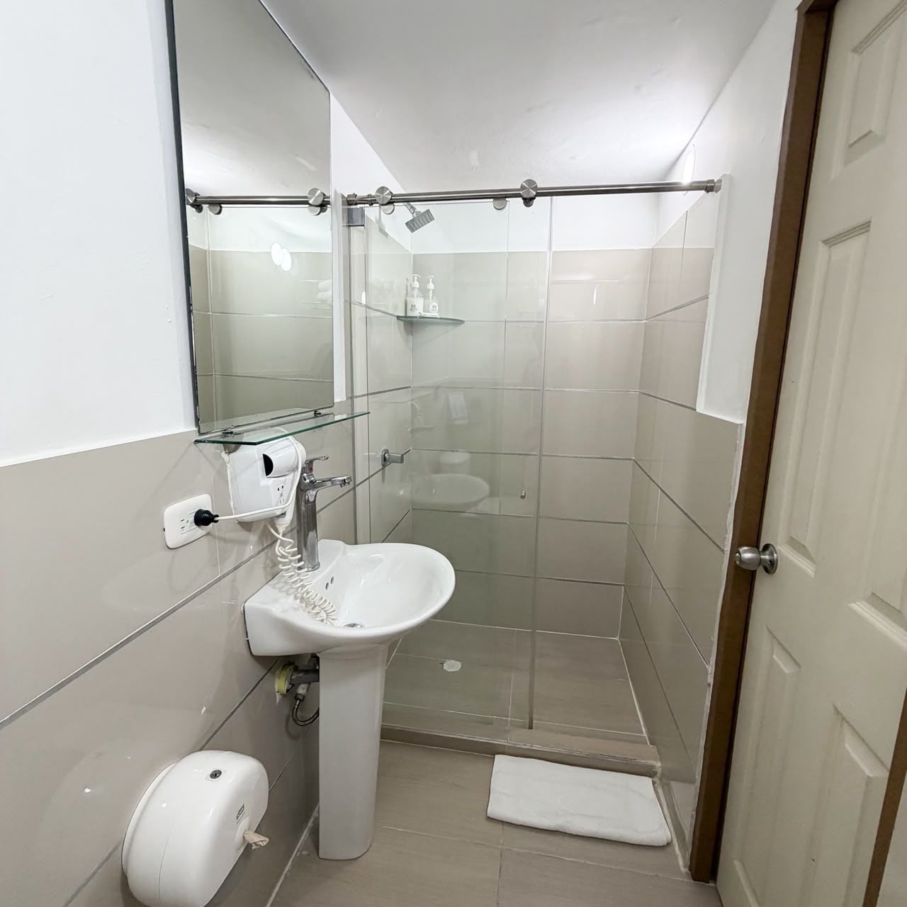 Un baño con cabina de ducha de vidrio, un lavabo blanco y un perchero para toallas.