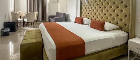 Habitación de hotel con una cama grande, una mesita de noche, una silla, un escritorio y una ventana con cortinas.