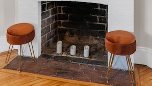 A white fireplace with a brick surround, two brown stools with gold legs, and a mirror above the fireplace. - Studio 1 ~ Lovely Apartment, Downtown! (Moncton)