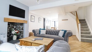 A modern living room with a grey sofa, a coffee table, a fireplace, and a staircase. - Neptune Cottage (Conwy)