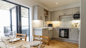 A modern kitchen with wooden flooring, white cabinets, and a dining area with a table set for two. - Neptune Cottage (Conwy)