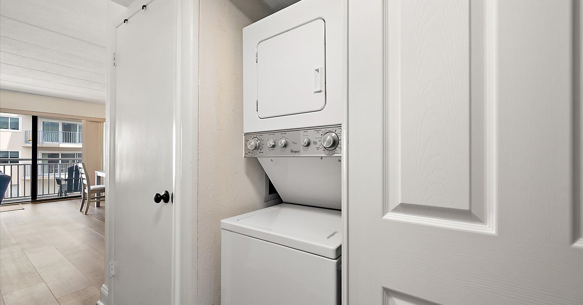 A laundry room with a washer and dryer, a door leading to a balcony, and a view of the outside.