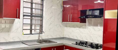 A compact kitchen with red cabinets, a built-in washing machine, a gas stove, and a window with a metal grill.