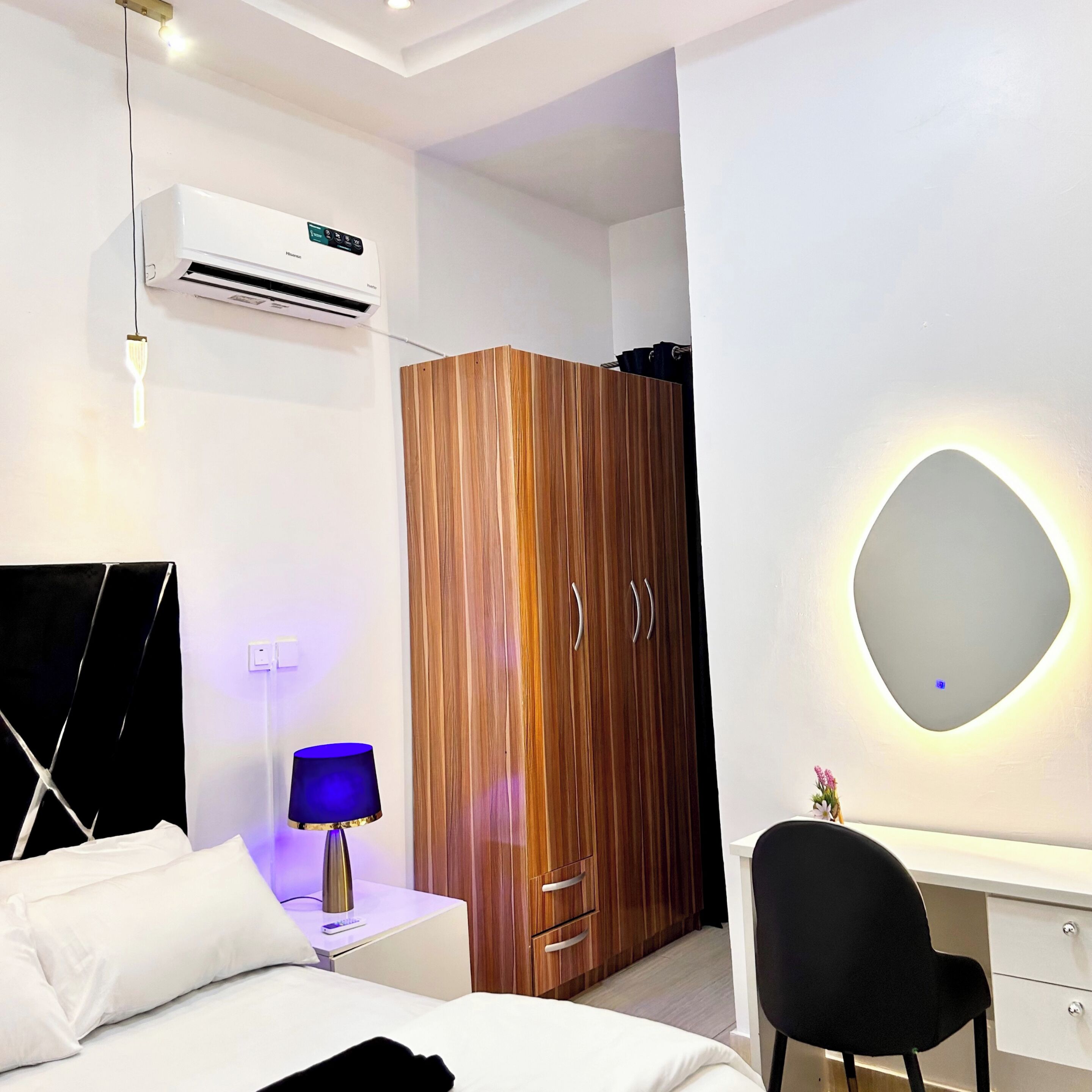 A modern bedroom with a bed, bedside table, lamp, wardrobe, and a desk with a chair.