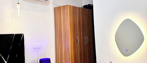 A modern bedroom with a bed, bedside table, lamp, wardrobe, and a desk with a chair.