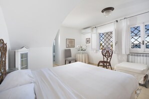 Een slaapkamer met een groot bed, een kleine tafel met een vaas, een stoel en een raam met gordijnen.