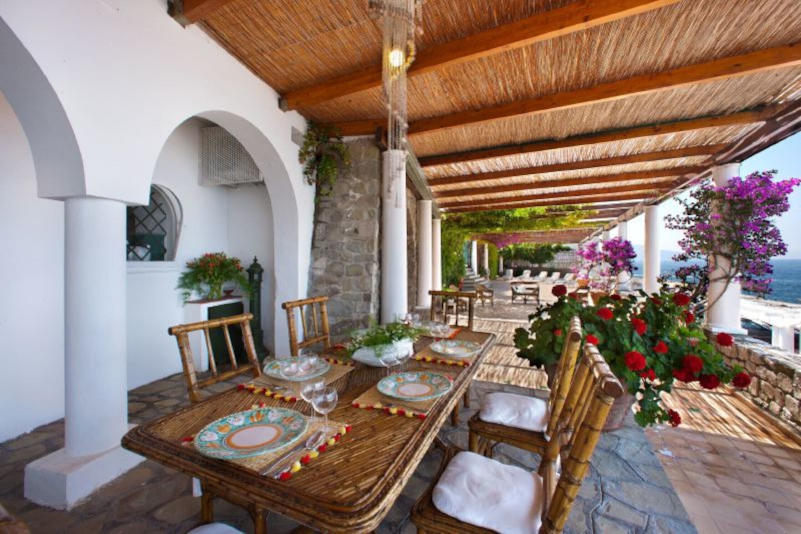An outdoor dining area with a thatched roof, stone columns, and a view of the sea.