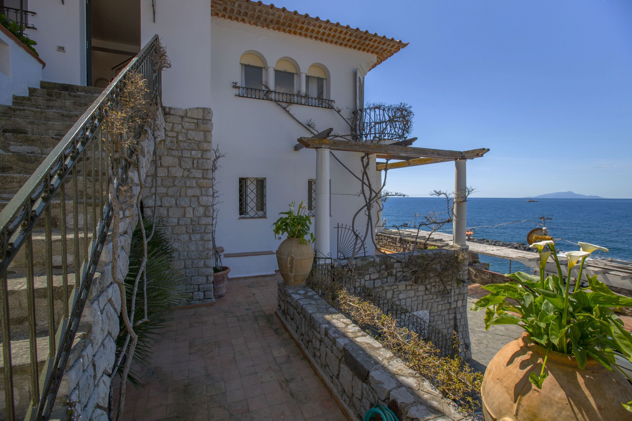 A coastal house with a stone staircase, a pergola, and a view of the sea.