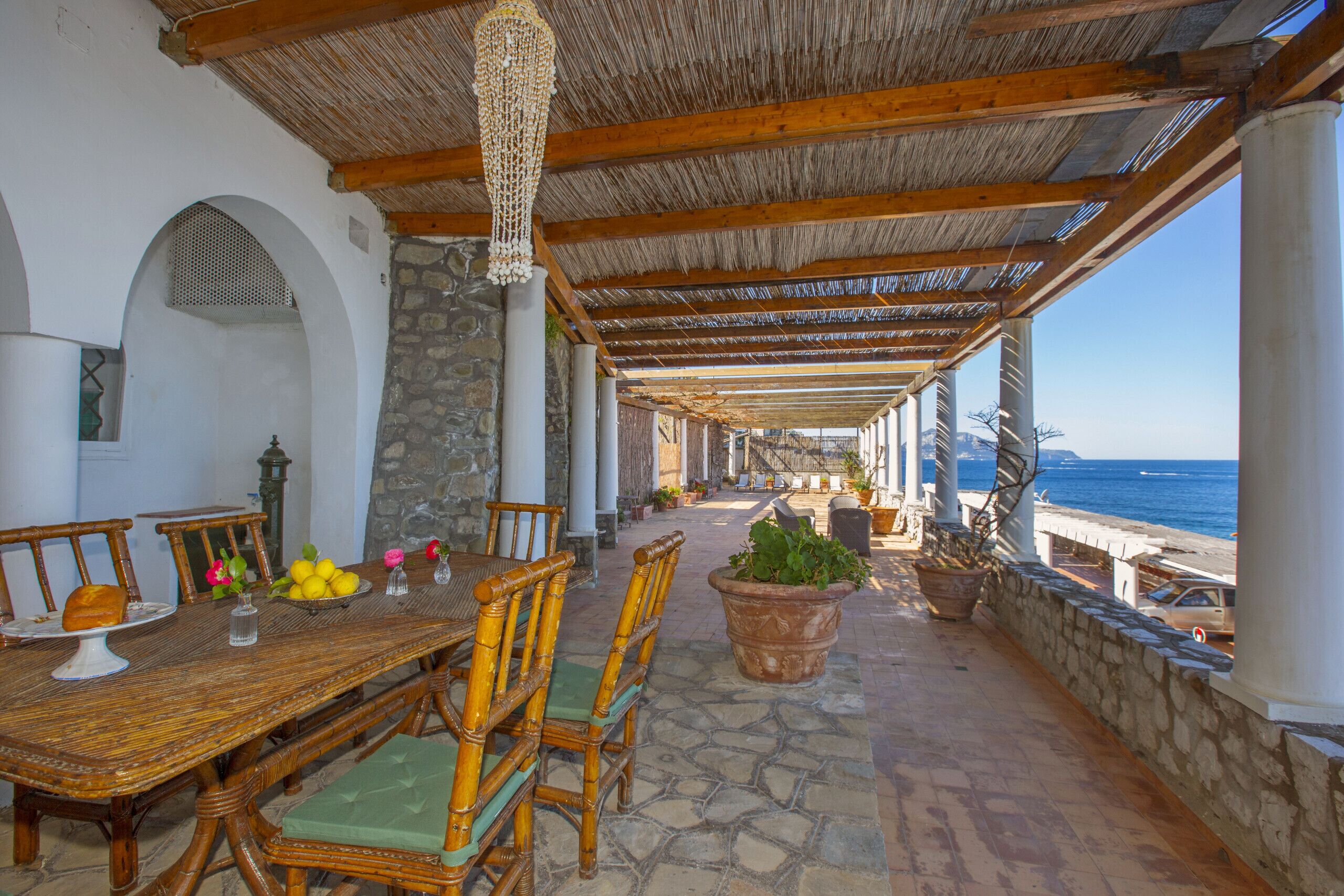 An outdoor dining area with a thatched roof, stone columns, and a view of the sea.