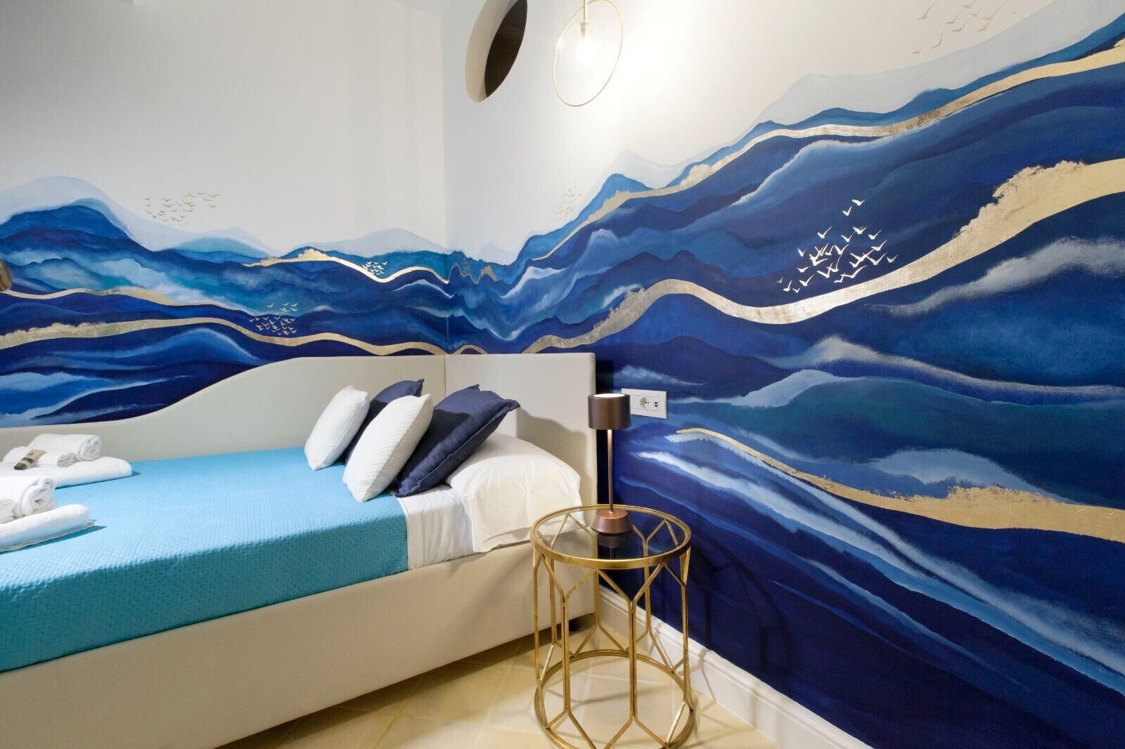 A bedroom with a bed, pillows, a bedside table, and a wall mural.
