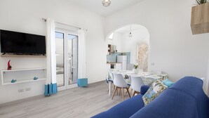 Un salon moderne avec un canapé bleu, un téléviseur à écran plat fixé au mur et un coin repas comprenant une table et des chaises.