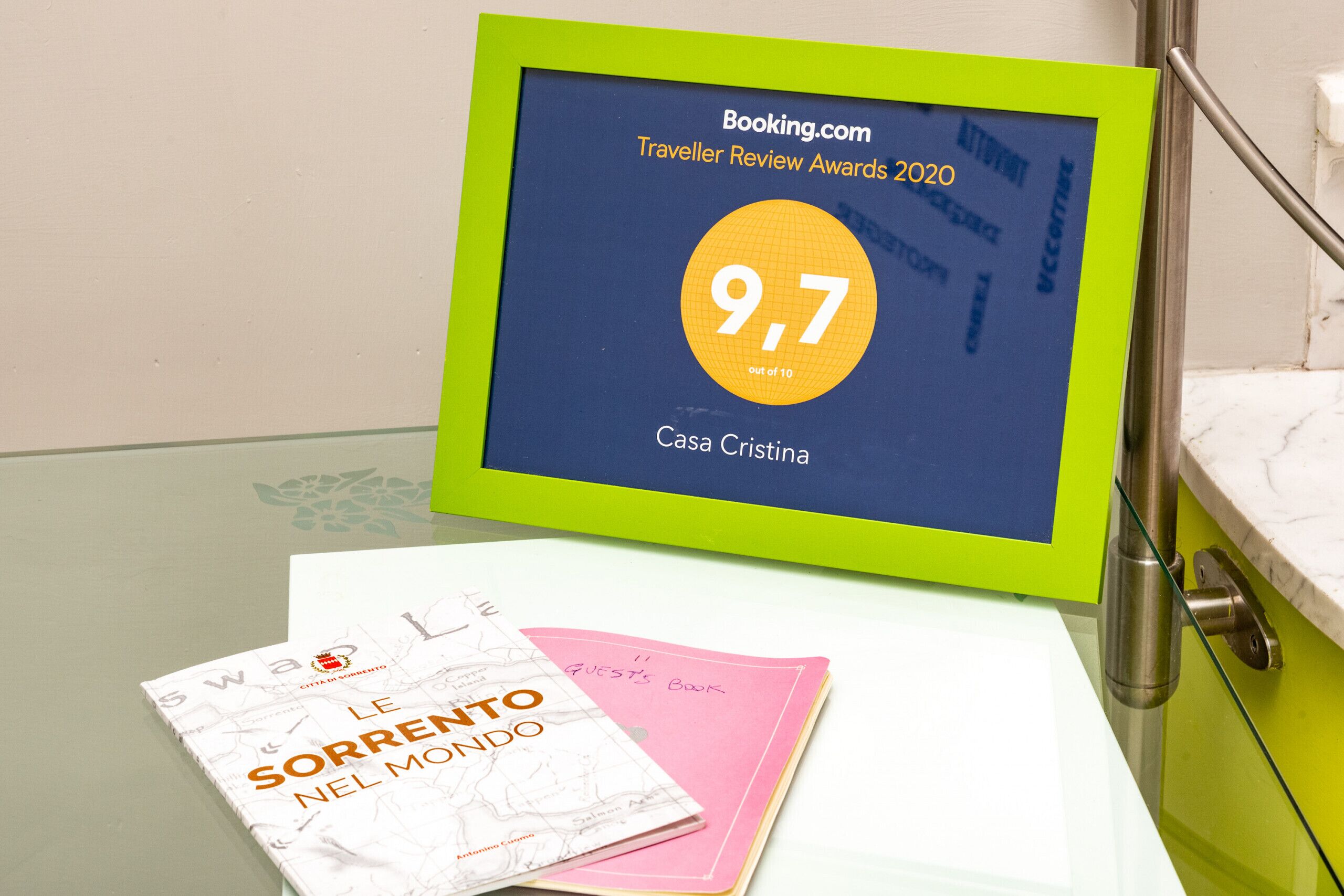 A digital display with a 9.7 rating for Casa Cristina, accompanied by a book titled "Le Sorrento nel mondo" and a pink notebook.