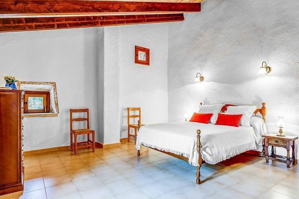 A bedroom with a wooden bed, two chairs, a nightstand, and a small table.