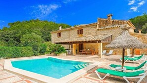 Eine Villa mit Swimmingpool, Sitzgelegenheiten im Freien und einem Strohdachschirm.