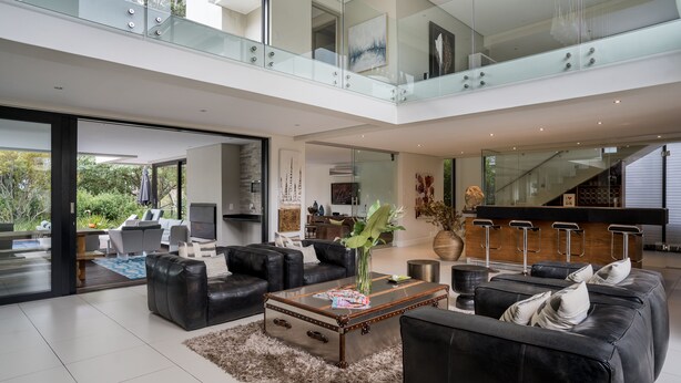 A spacious living area with leather sofas, a coffee table, and a glass railing overlooking a garden.