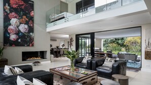 A spacious living room with a black leather sofa, a glass coffee table, and a large floral painting.