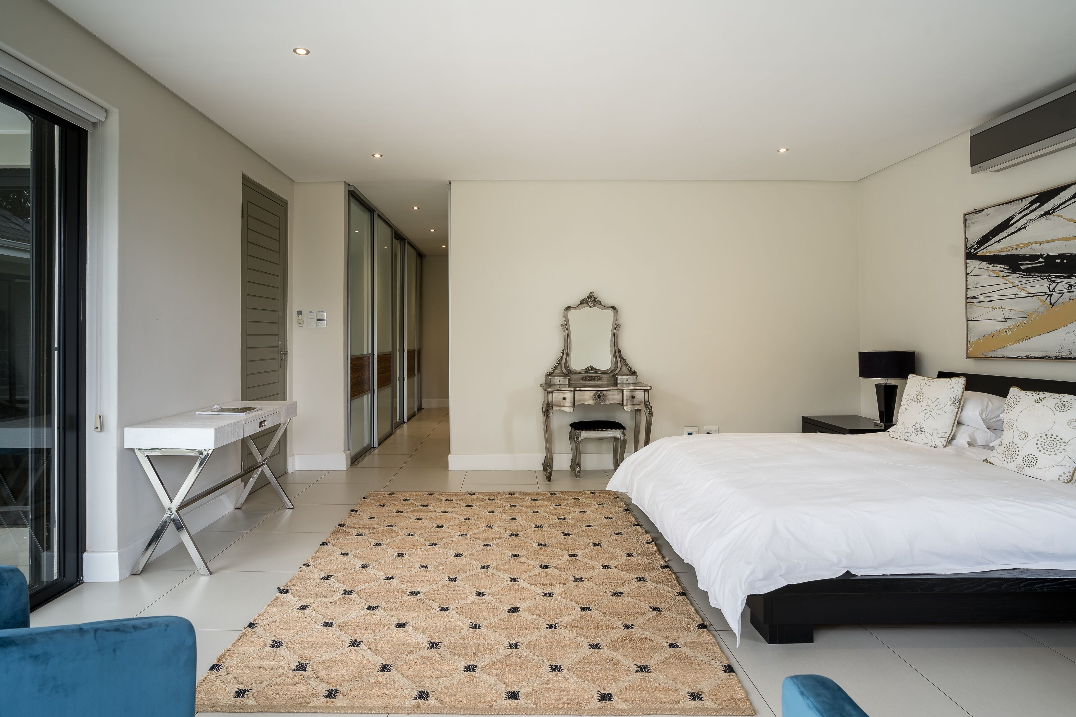 A bedroom with a bed, bedside table, dresser, mirror, and a view of a hallway.