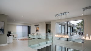A modern living room with a glass railing, a white sofa, and a dining area with a view of the outdoors.