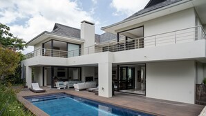 A modern two-story house with a swimming pool, outdoor seating, and a balcony.