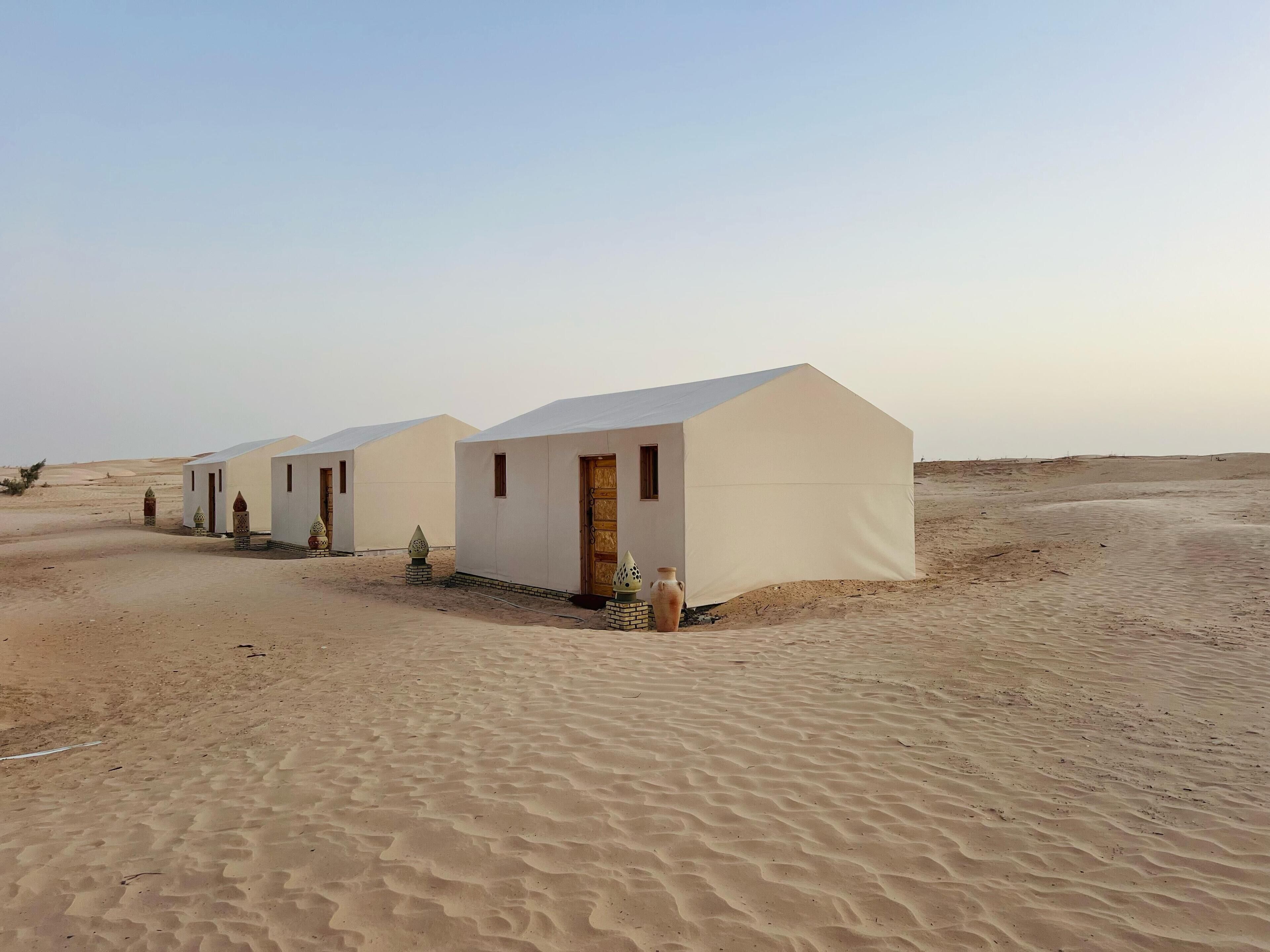 A row of white tents with flat roofs, arranged in a desert setting.