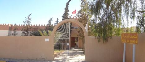 A museum entrance with a metal gate, a flag, and a sign in a foreign language.