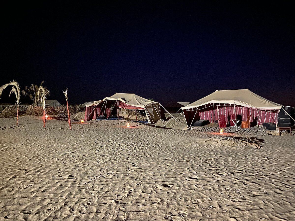 A series of tents on a sandy beach at night, with some lights visible.
