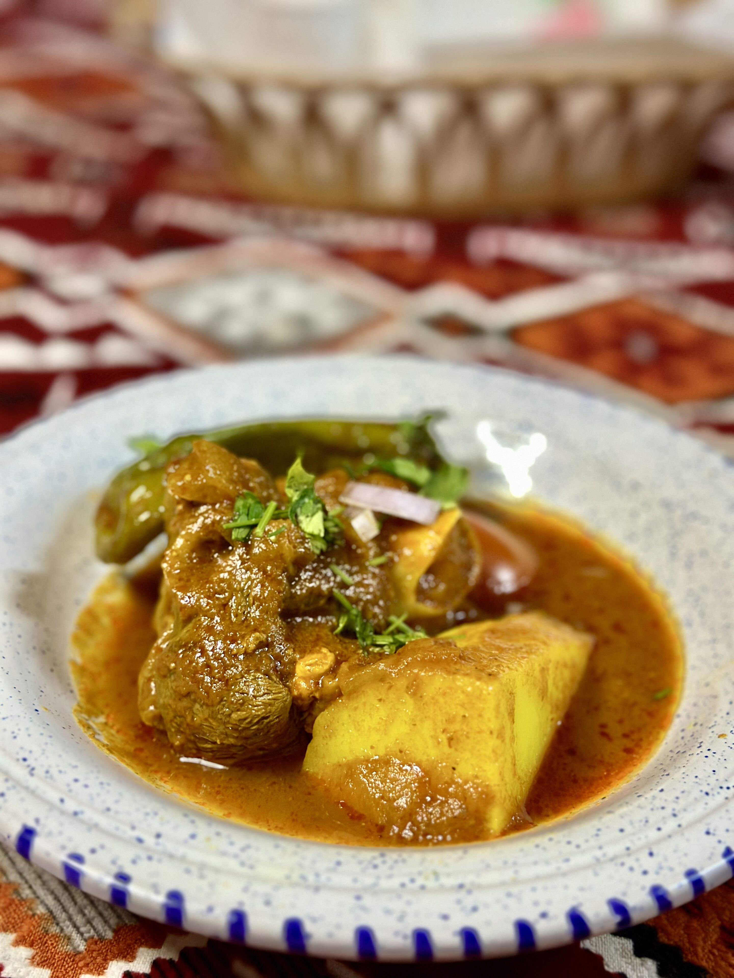 A plate of curry with meat and potatoes, garnished with herbs.
