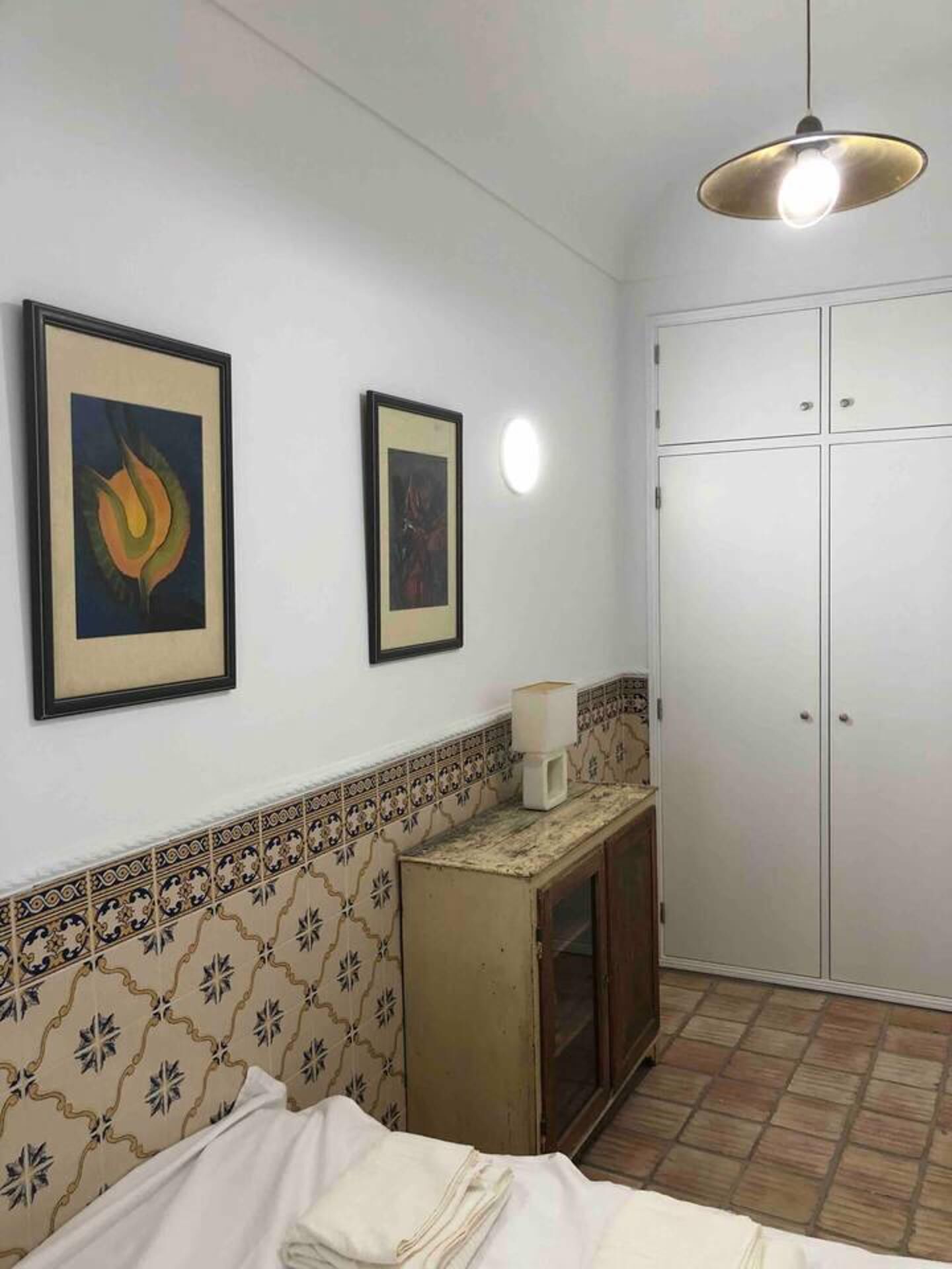 A room with a bed, a cabinet, and a wardrobe. There are two framed pictures on the wall.