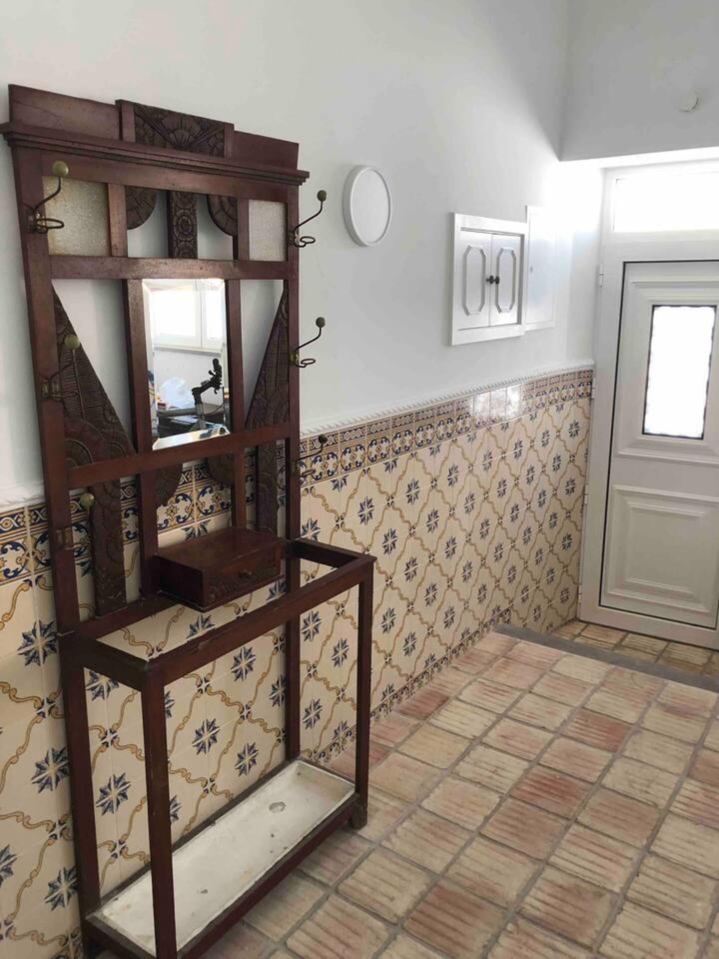 A bathroom with a tiled floor, a wooden shelf unit, a mirror, and a white door.