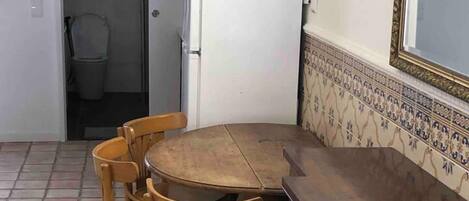 A small kitchen with a round wooden table and four wooden chairs. A white refrigerator is visible in the background.