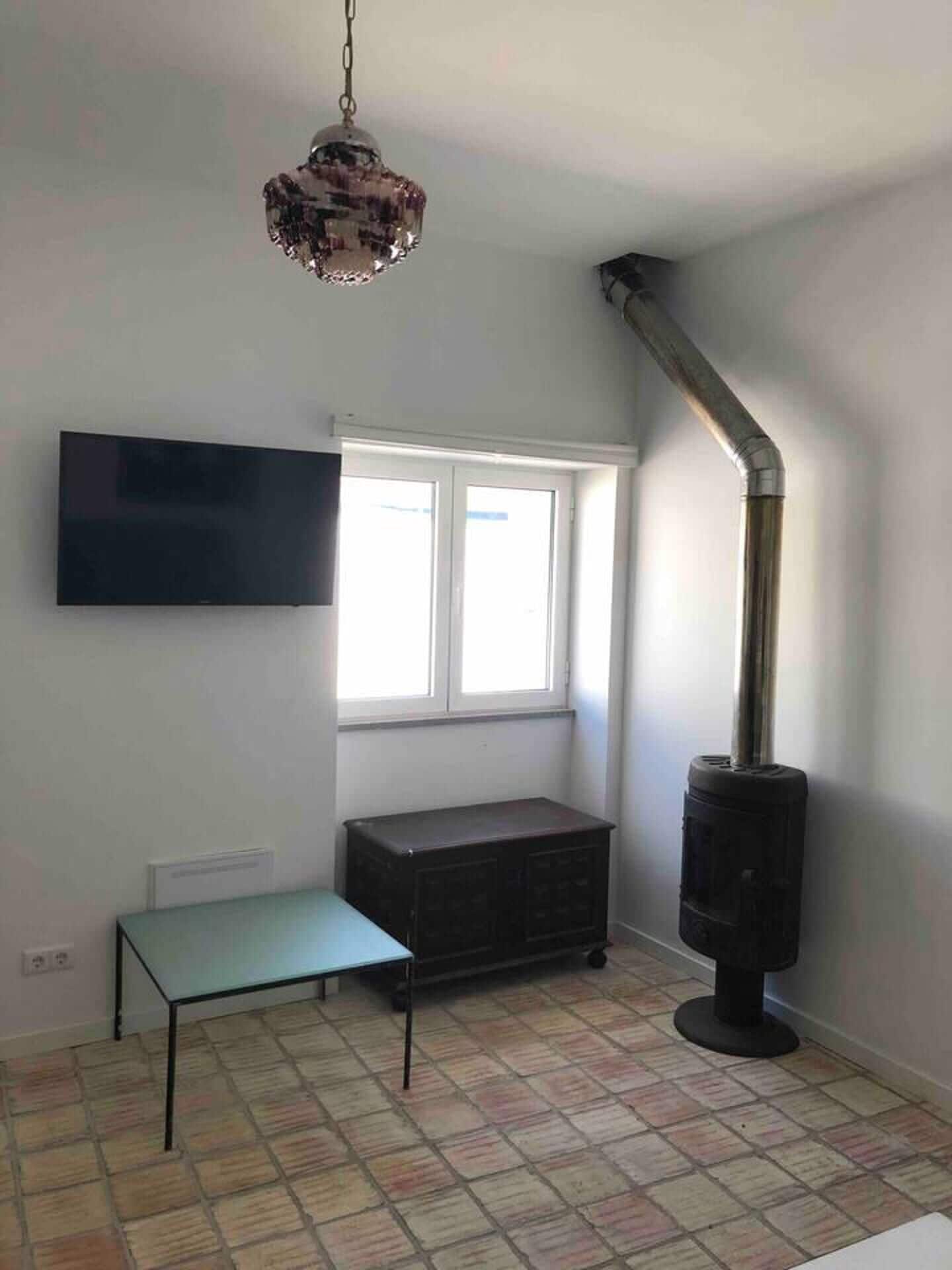 Une pièce avec un sol carrelé, un banc, un téléviseur fixé au mur, une fenêtre et une cheminée.