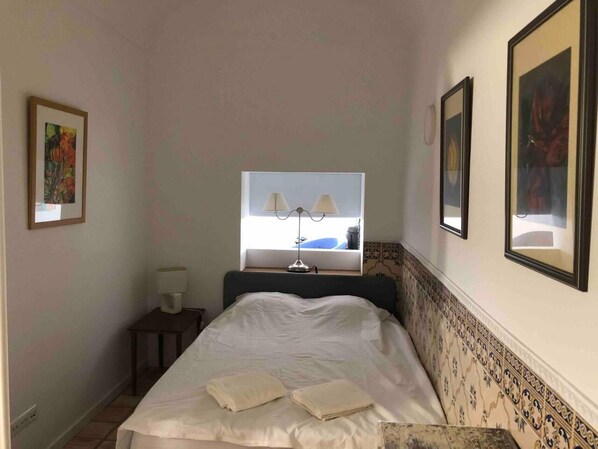 A bedroom with a bed, a nightstand, a lamp, and two framed pictures on the wall. - Stunning Fishermans House in Central Fuseta (Olhao)