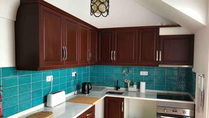 A kitchen with dark wooden cabinets, a teal backsplash, a stainless steel oven, and a green trash bin. - Stunning Fishermans House in Central Fuseta (Olhao)