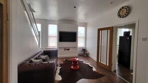 Un salon moderne avec un canapé en cuir, un téléviseur à écran plat, un plancher en bois et un tapis en peau de vache.