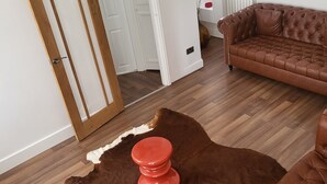 Un salon avec un canapé en cuir marron, un pouf rouge et un tapis en peau de vache.