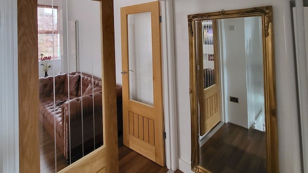 Un couloir orné d’un lustre, doté de portes en bois et d’un miroir.