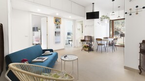 Een ruime woonkamer met een blauwe bank, een rieten fauteuil en een eettafel met stoelen.