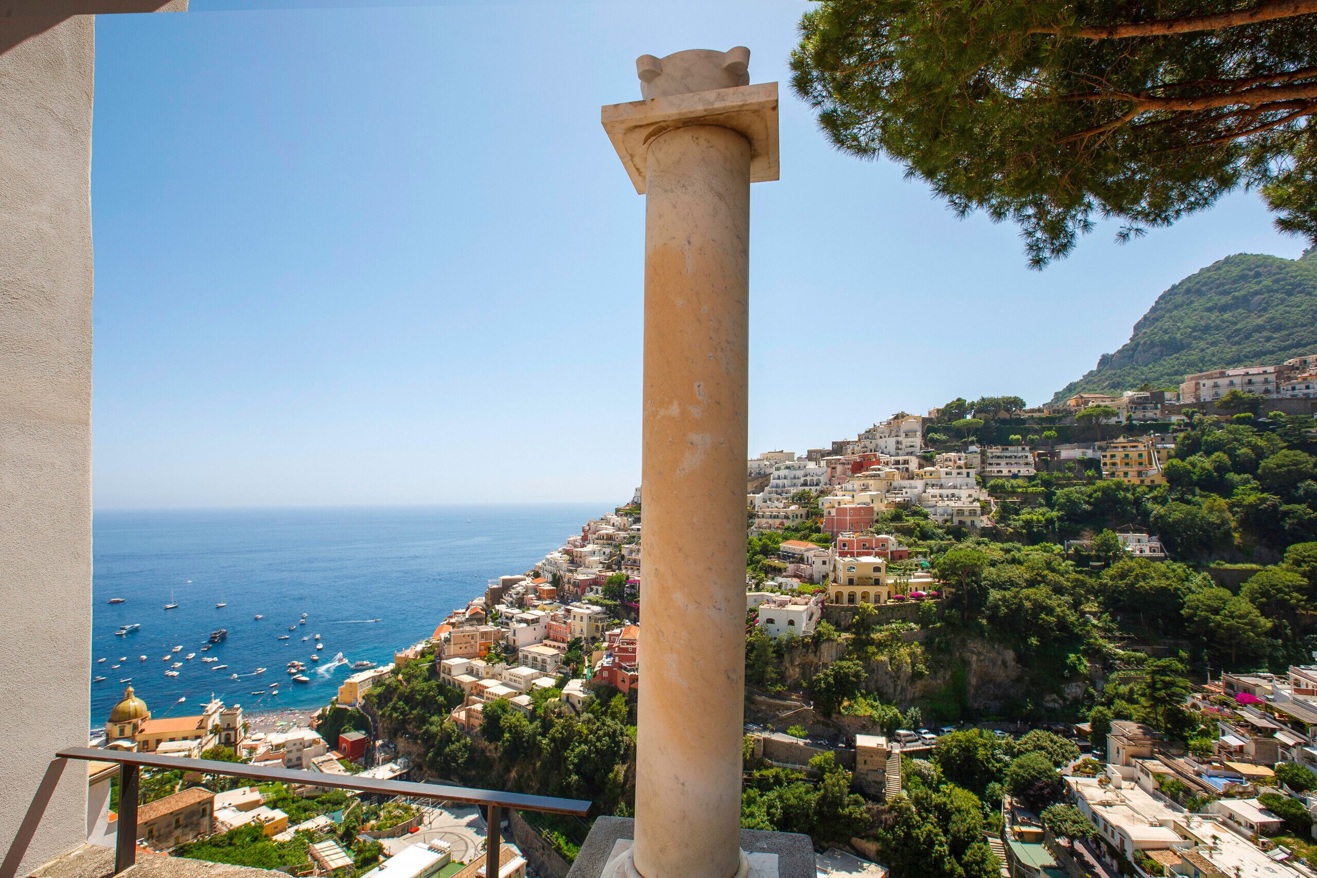Un pueblo costero con una columna destacada, edificios y barcos en el mar.