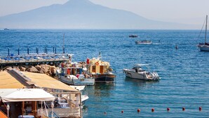 Un port de plaisance avec des bateaux amarrés, une jetée avec des chaises, et une montagne en arrière-plan.